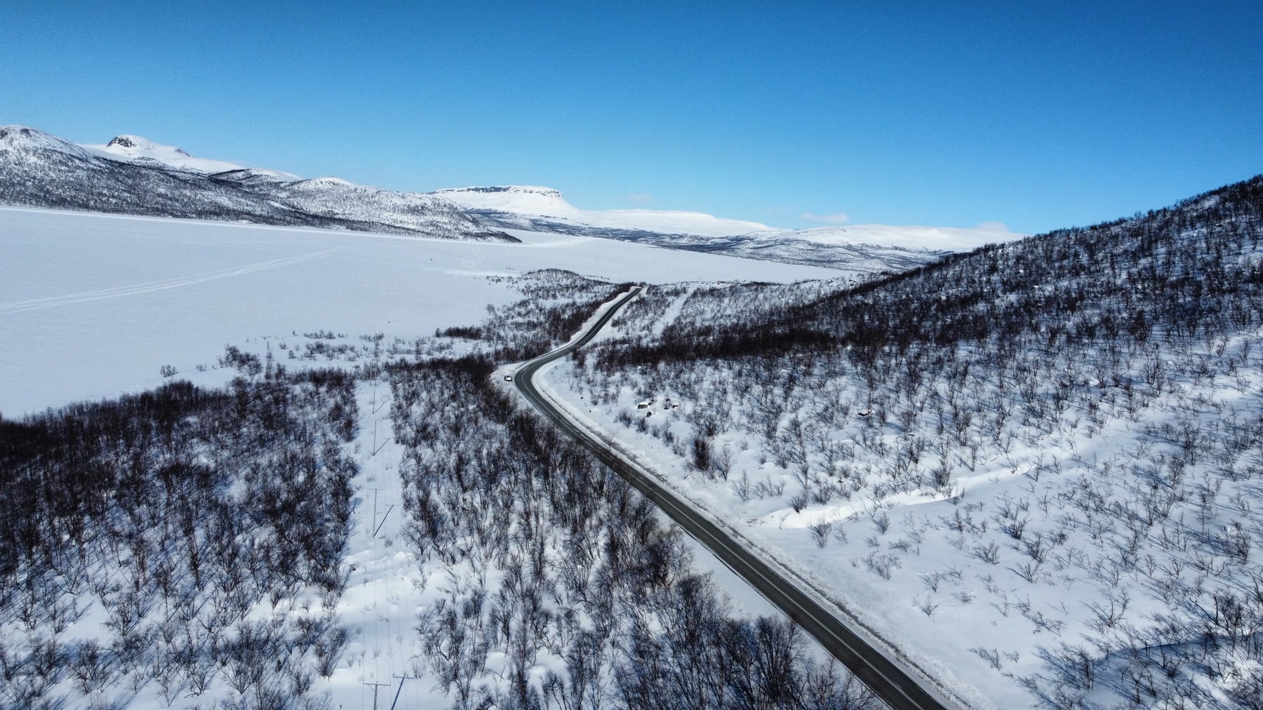 Vista aérea de una carretera entre montañas y bosques cubiertos de nieve