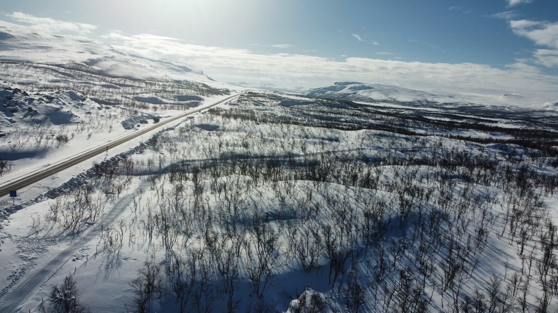 Carretera atravesando una meseta de montañas nevadas bajo el sol