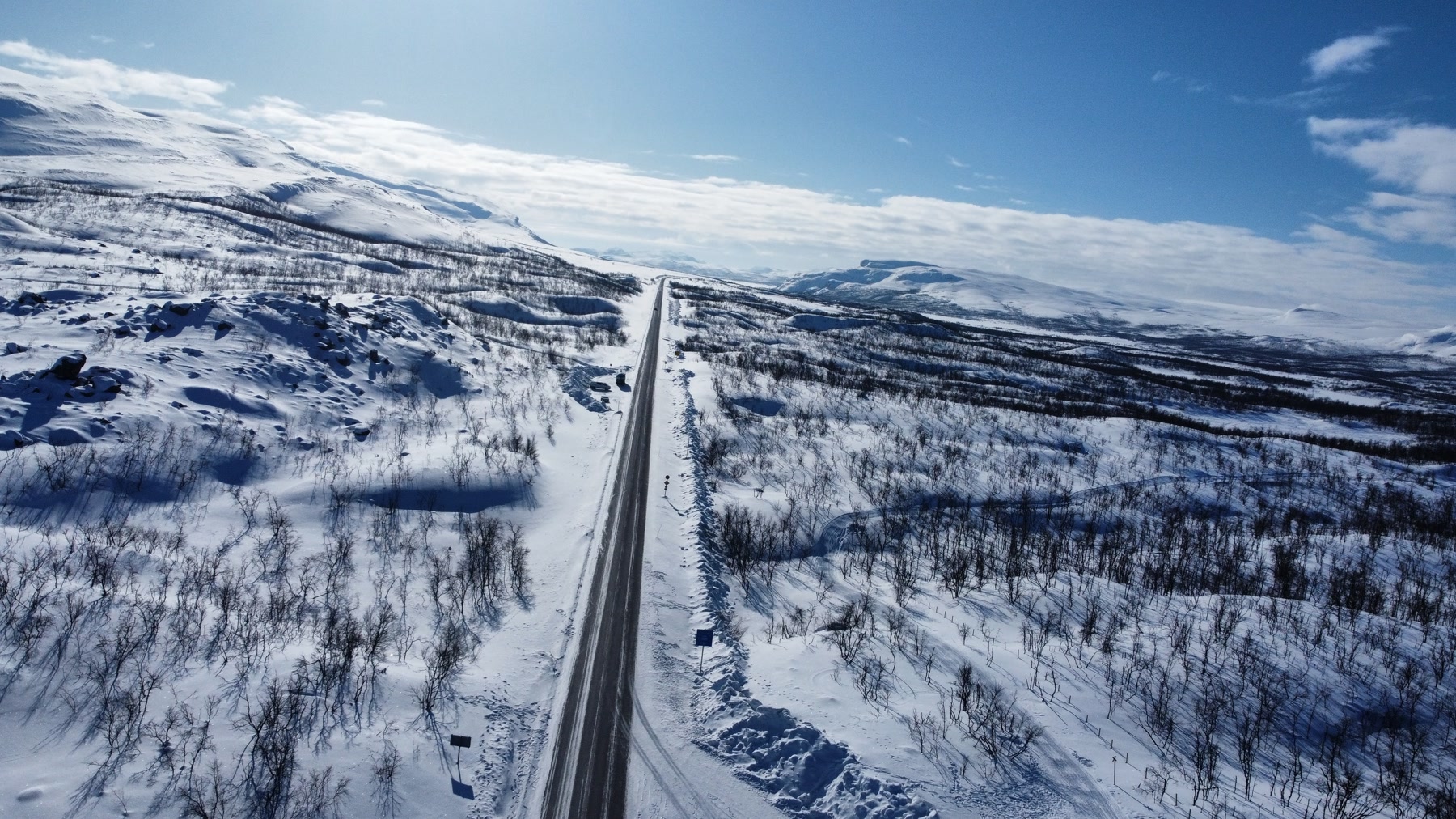 Carretera recta avanzando entre colinas y vegetación cubierta de nieve