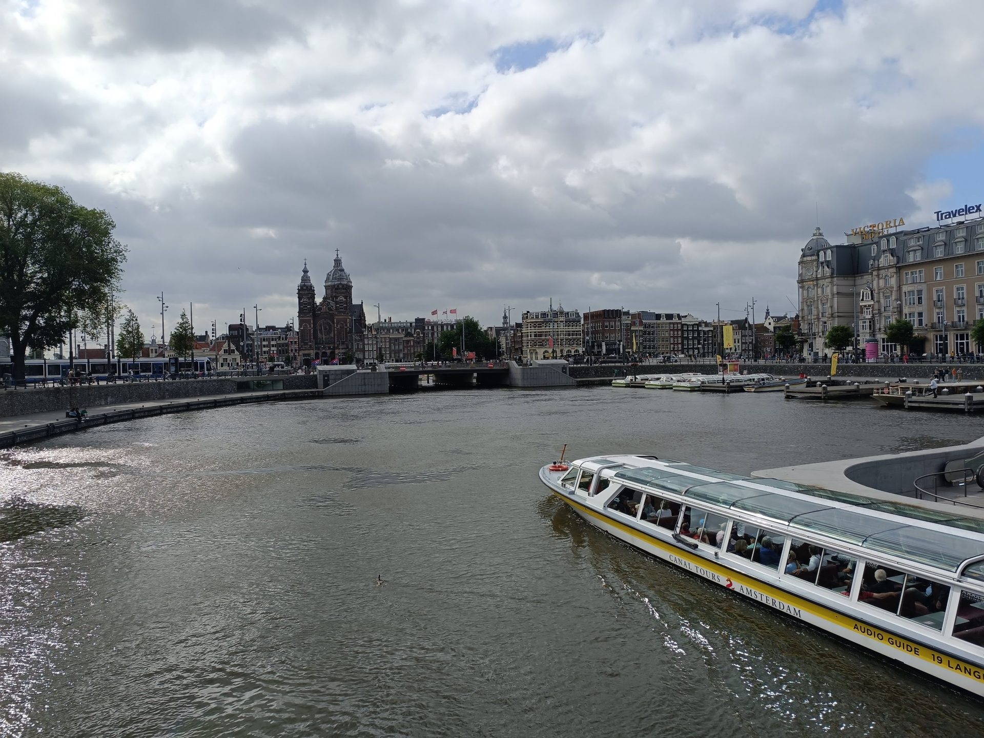 Barco turístico en la bahía frente a la estación central de Ámsterdam, con la basílica de San Nicolás al fondo