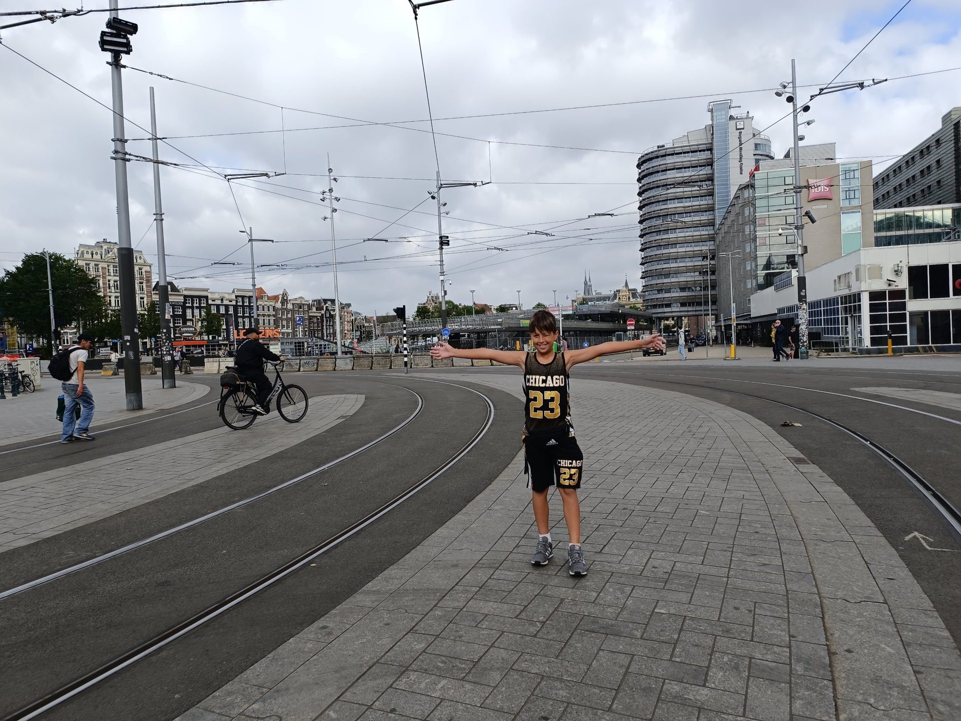 Niño con los brazos abiertos entre las vías del tranvía frente a la estación central de Ámsterdam