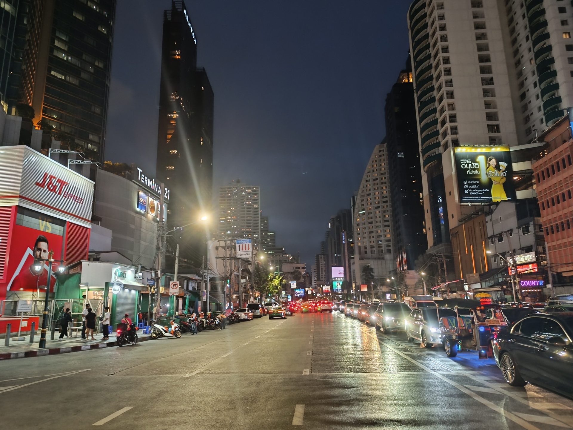 Avenida de Bangkok de noche con el asfalto mojado, tráfico y rascacielos iluminados