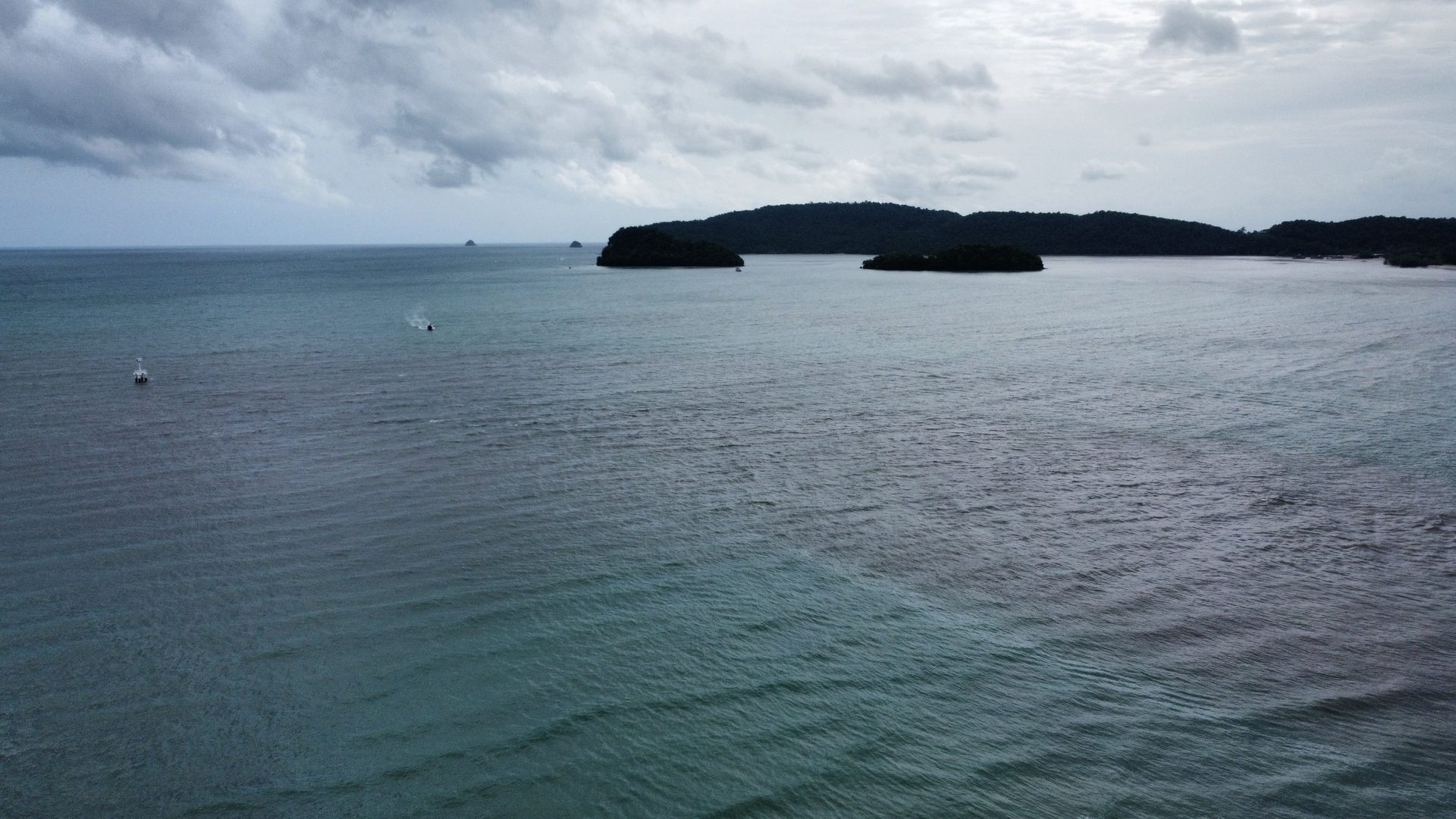 Mar abierto de Krabi desde el dron con una lancha dejando estela frente a dos islotes