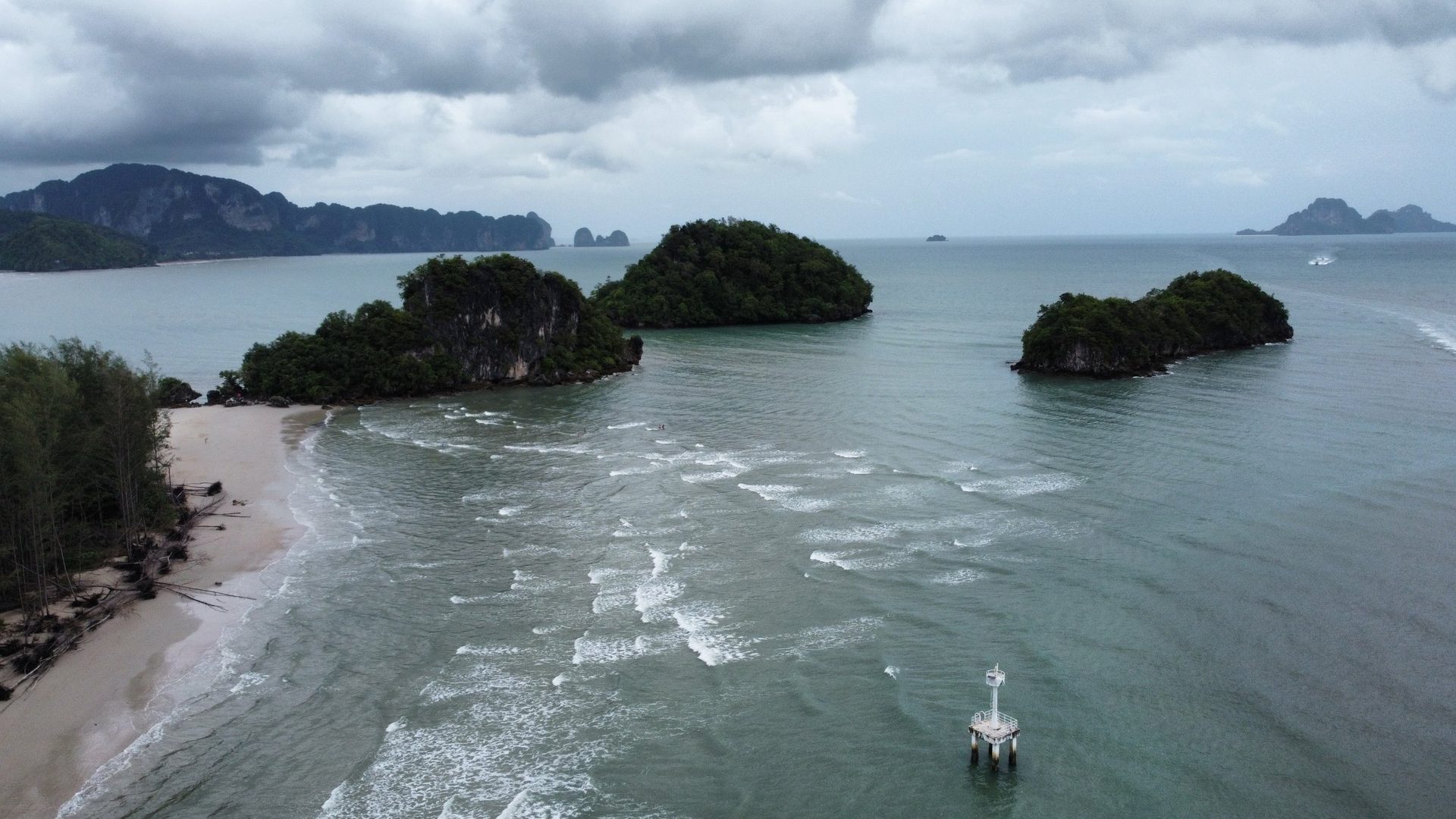 Vista de dron de tres islotes de caliza frente a una playa de Krabi, con una baliza blanca en el agua