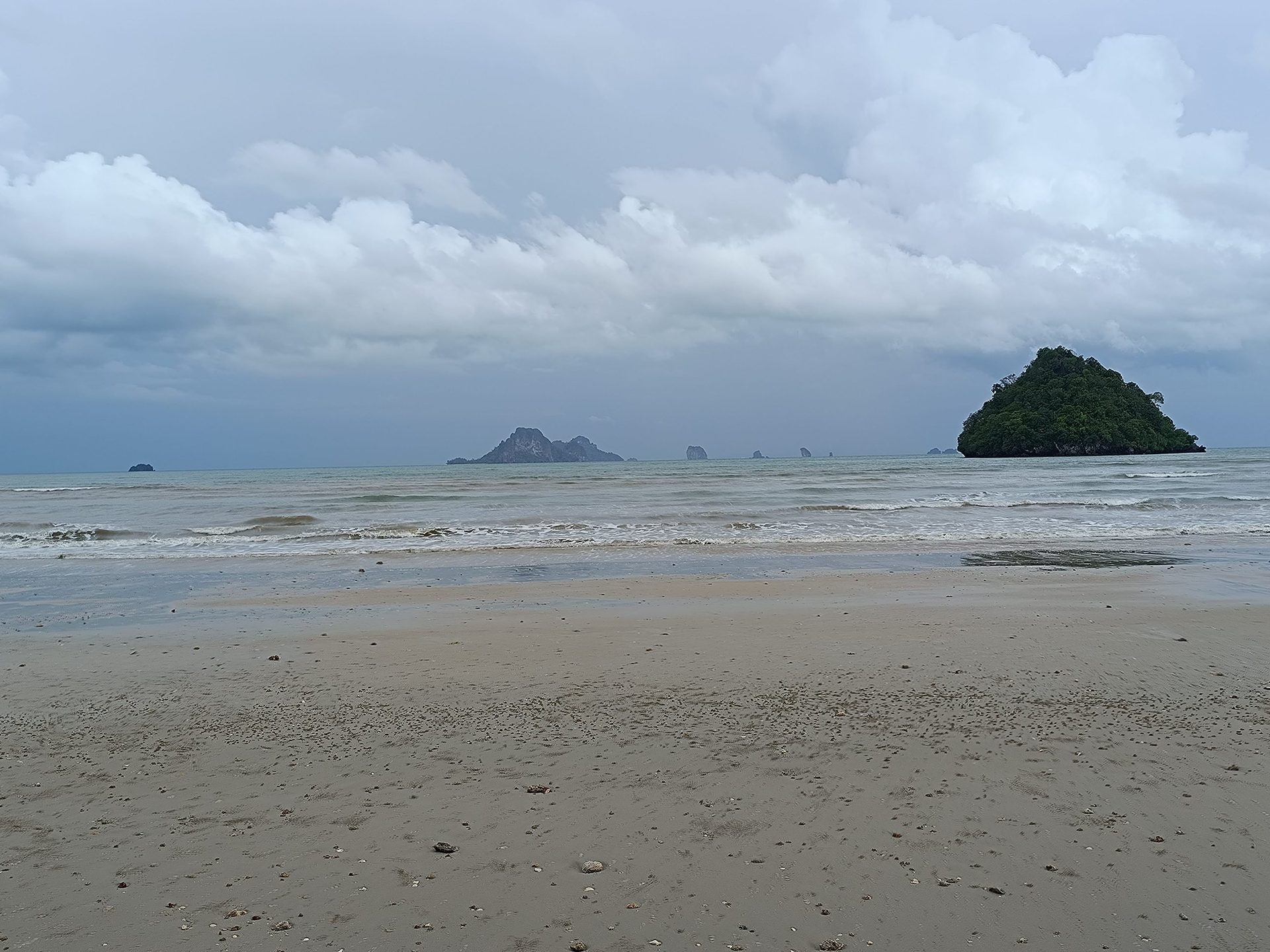 Playa de arena mojada en Krabi con un islote cubierto de selva y peñones en el horizonte
