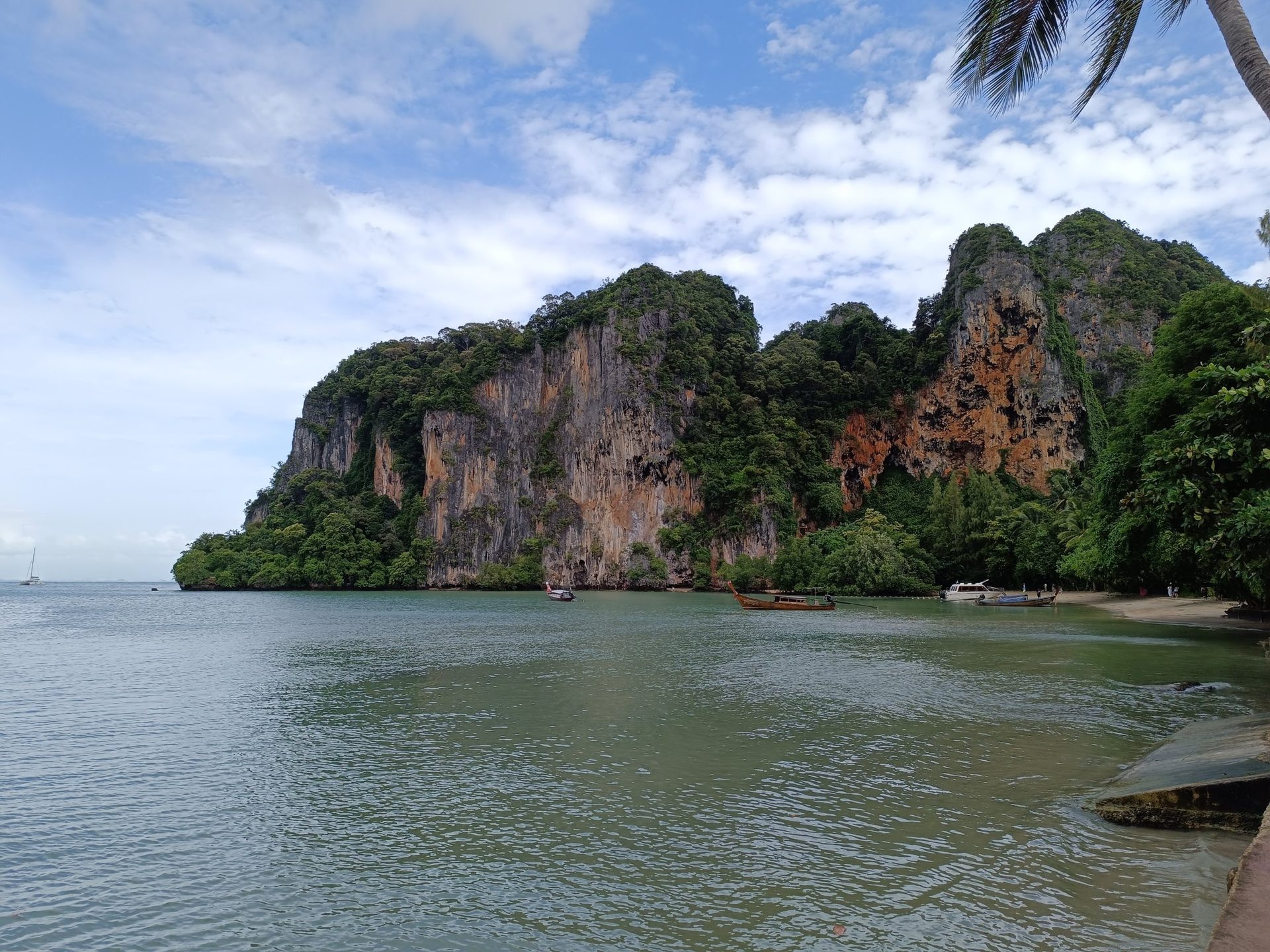 Acantilados de caliza naranja y gris cubiertos de selva sobre una bahía con barcas de cola larga en Railay
