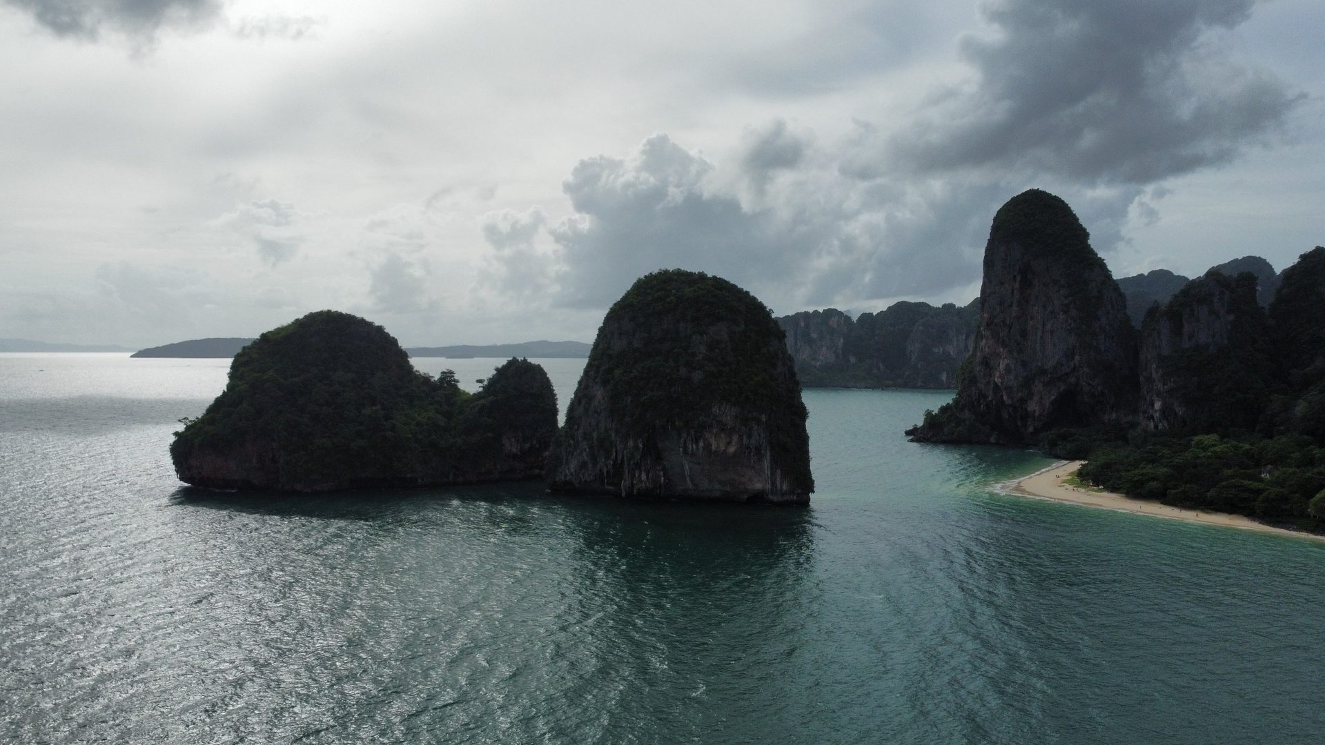 Peñones de caliza oscuros sobre el mar de Railay bajo un cielo de tormenta, con una playa a la derecha