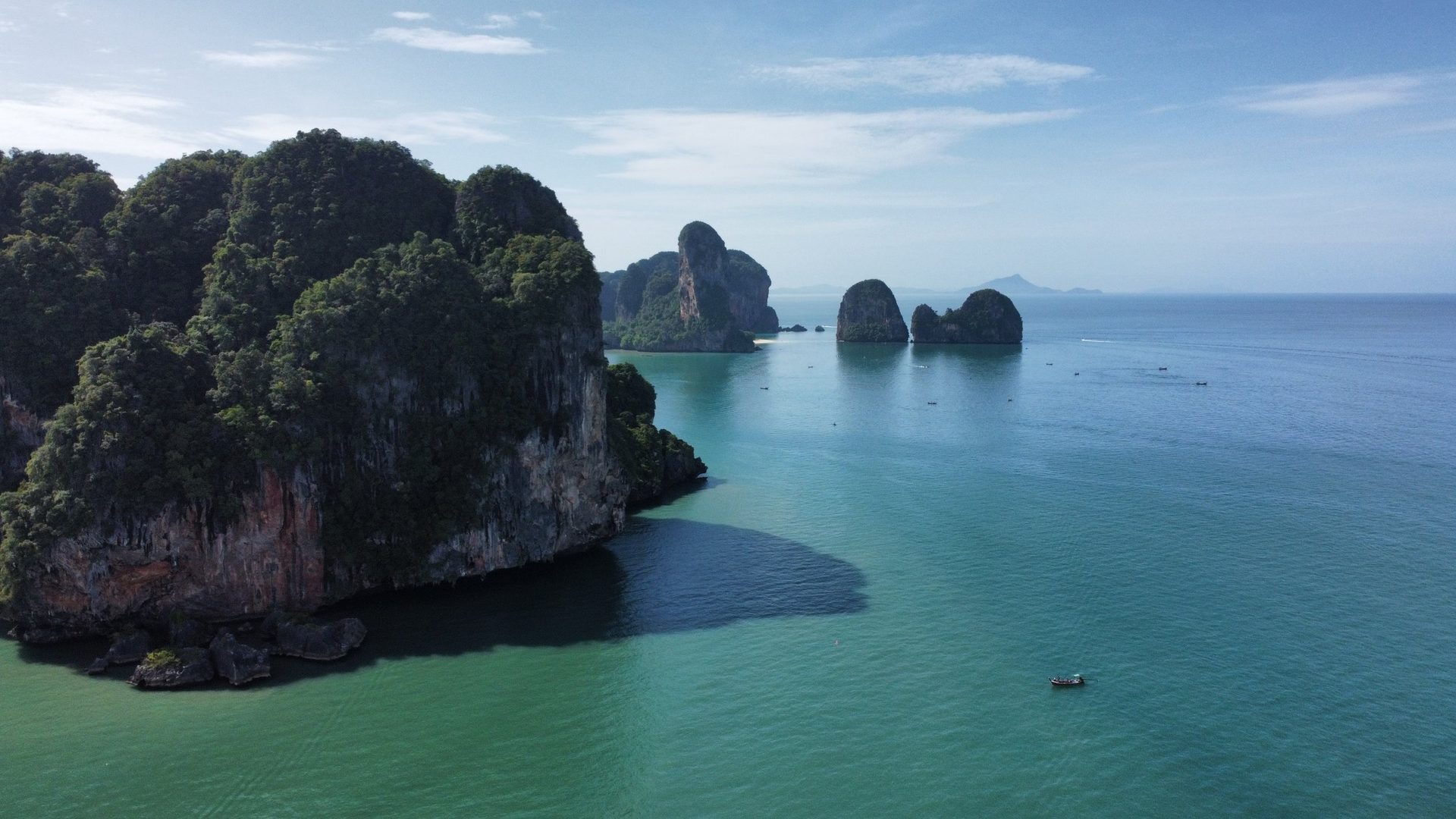 Vista de dron de los acantilados de Railay sobre agua turquesa, con peñones de caliza en el mar y una barca de cola larga