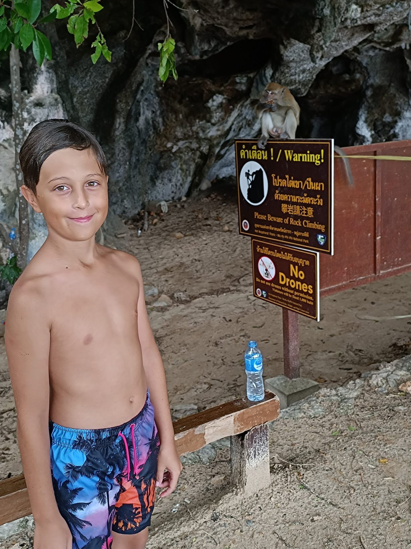 Niño sonriendo junto a un cartel del parque nacional mientras un macaco come sentado encima